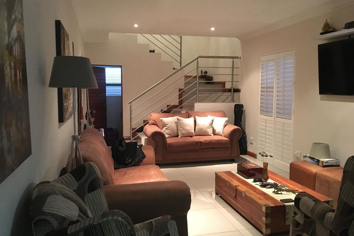 Spacious living room featuring tiled flooring, recessed lighting, and a modern staircase with a stainless steel balustrade, complemented by plantation shutters.