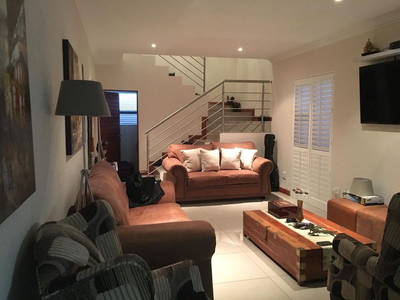 Spacious living room featuring tiled flooring, recessed lighting, and a modern staircase with a stainless steel balustrade, complemented by plantation shutters.