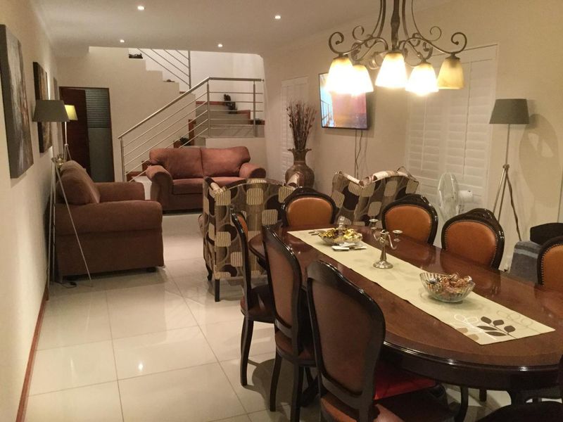 Spacious open-plan living and dining area featuring polished porcelain floor tiles, recessed lighting, and a modern staircase with a stainless steel balustrade.