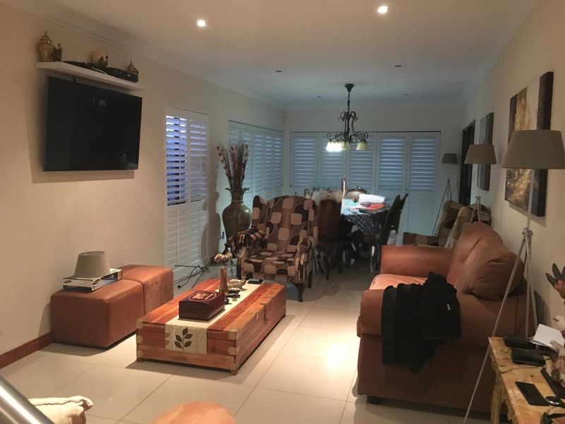 Spacious open-plan living and dining area featuring neutral tiled flooring, recessed downlighting, and white plantation shutters throughout.