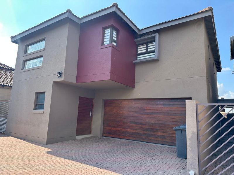 Modern townhouse exterior featuring a double-story facade, timber garage door, paved driveway, and secure gated entrance.