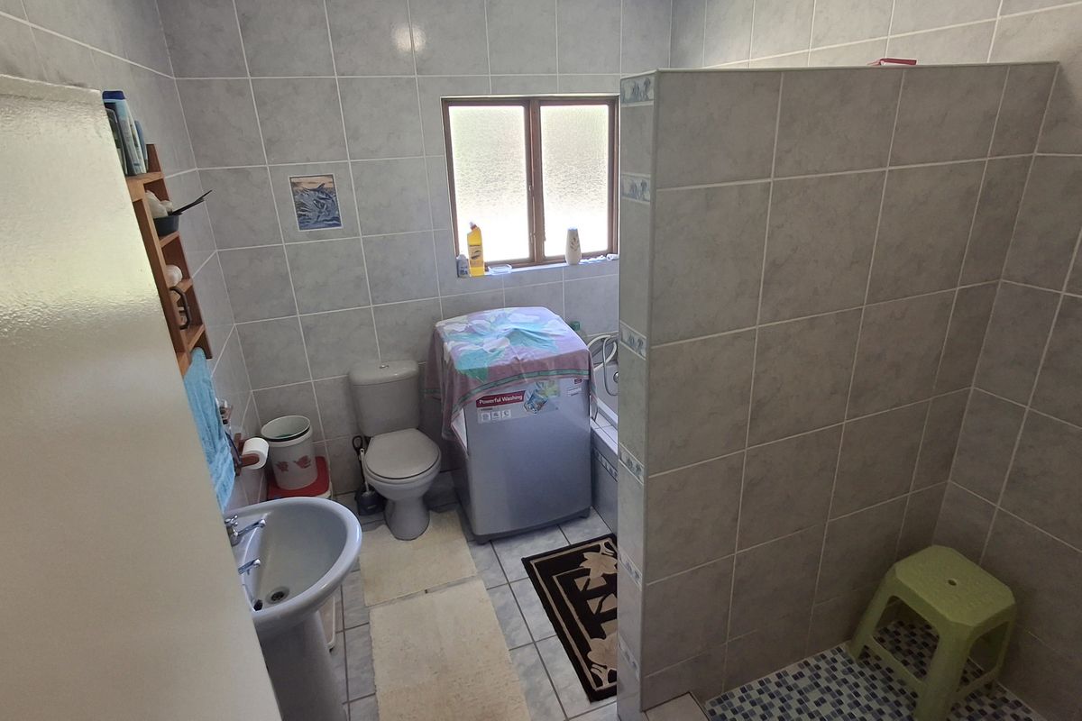 A functional bathroom featuring a pedestal basin, toilet, and a tiled shower enclosure with a privacy wall.