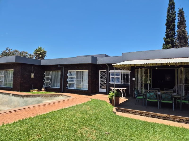 Rear view of the property featuring a brick facade, a covered patio area, and an adjacent swimming pool set within a landscaped garden.