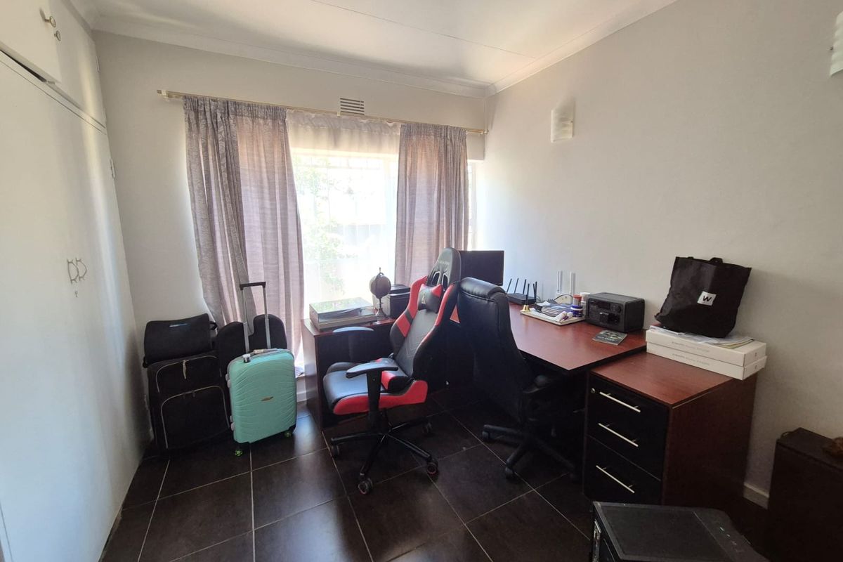 A functional bedroom featuring tiled flooring and built-in cupboards, currently utilized as a home office space.