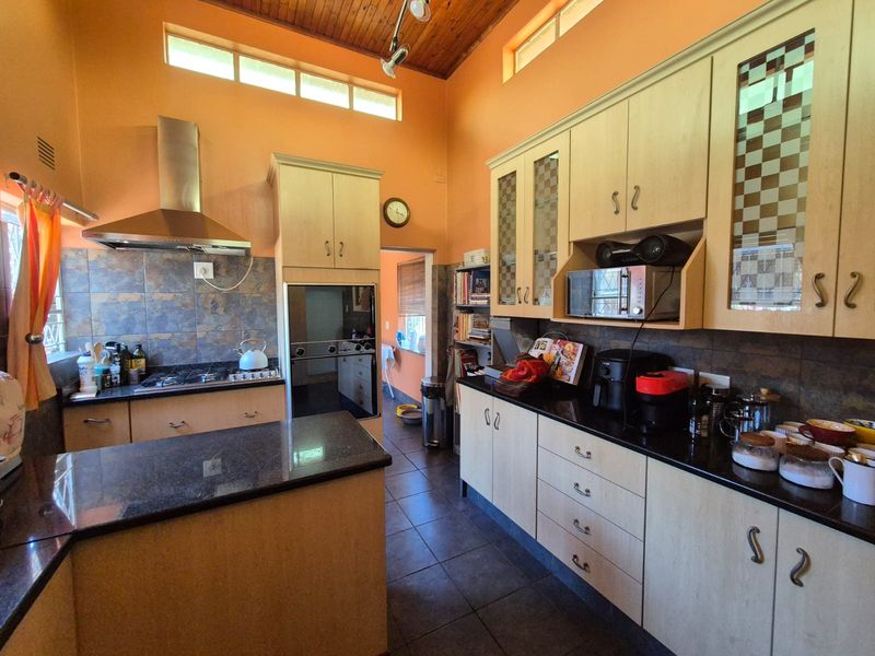 A functional kitchen featuring timber cabinetry, granite countertops, built-in oven, gas hob, and a high timber-clad ceiling with clerestory windows for natural light.