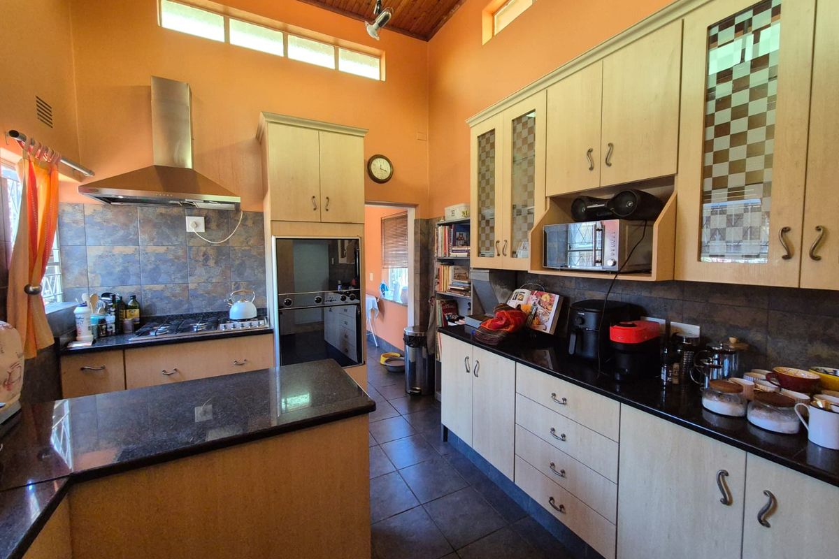 A functional kitchen featuring timber cabinetry, granite countertops, built-in oven, gas hob, and a high timber-clad ceiling with clerestory windows for natural light.