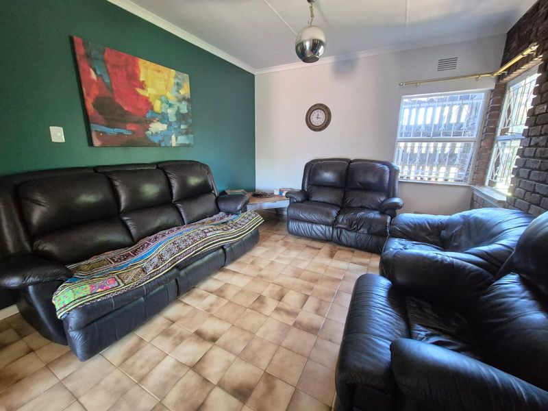 A living room featuring ceramic tile flooring, an exposed brick feature wall, and a bold green accent wall with security bars on the windows.