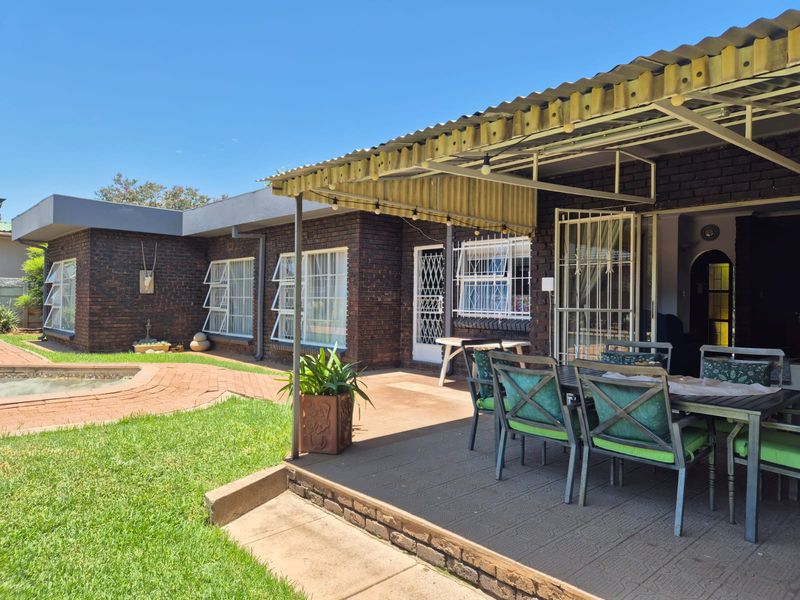 A covered outdoor patio area featuring brick construction, paved flooring, and direct access to the garden and swimming pool.