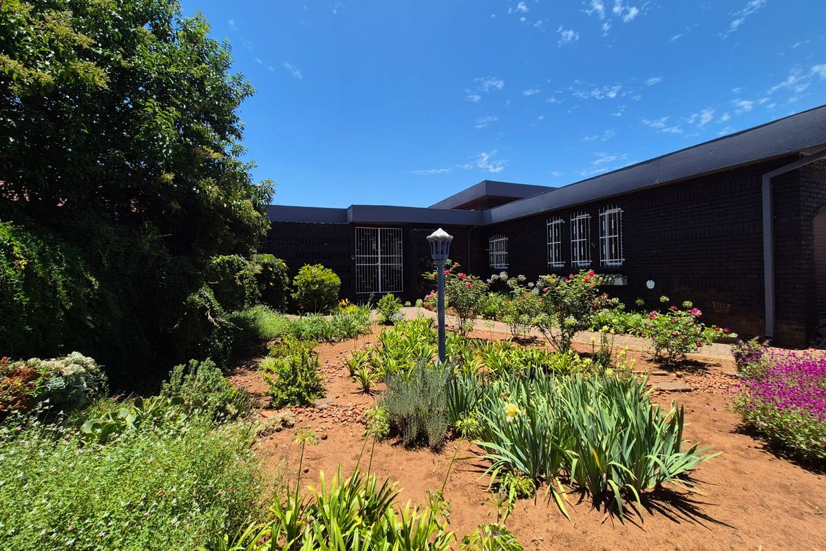 A rear view of the property featuring a dark brick facade with security bars and a well-established garden with a central lamp post.