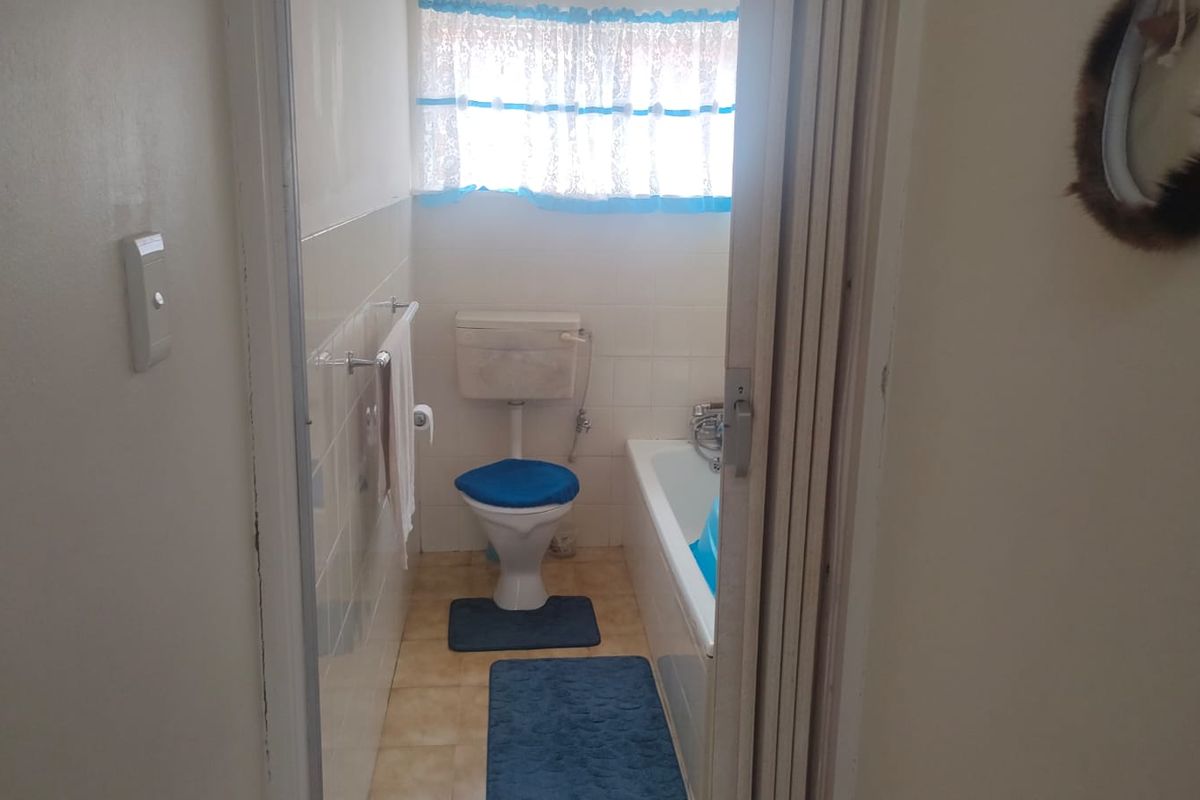 A functional bathroom featuring a standard bathtub, toilet, and tiled finishes, offering potential for modernization and cosmetic updates.