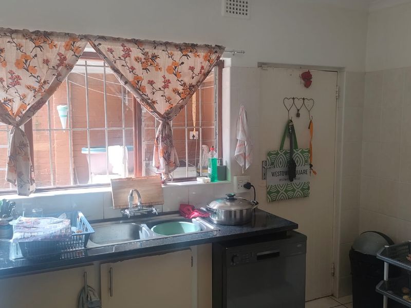 Functional kitchen area featuring a double bowl sink, granite countertops, tiled backsplash, and a window with security bars.