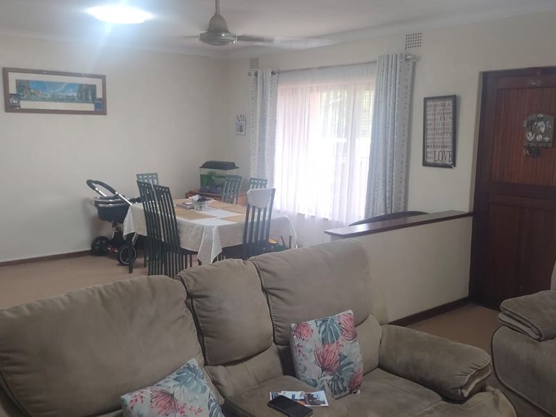 Open plan living and dining area featuring a ceiling fan, neutral wall finishes, and a timber entrance door.