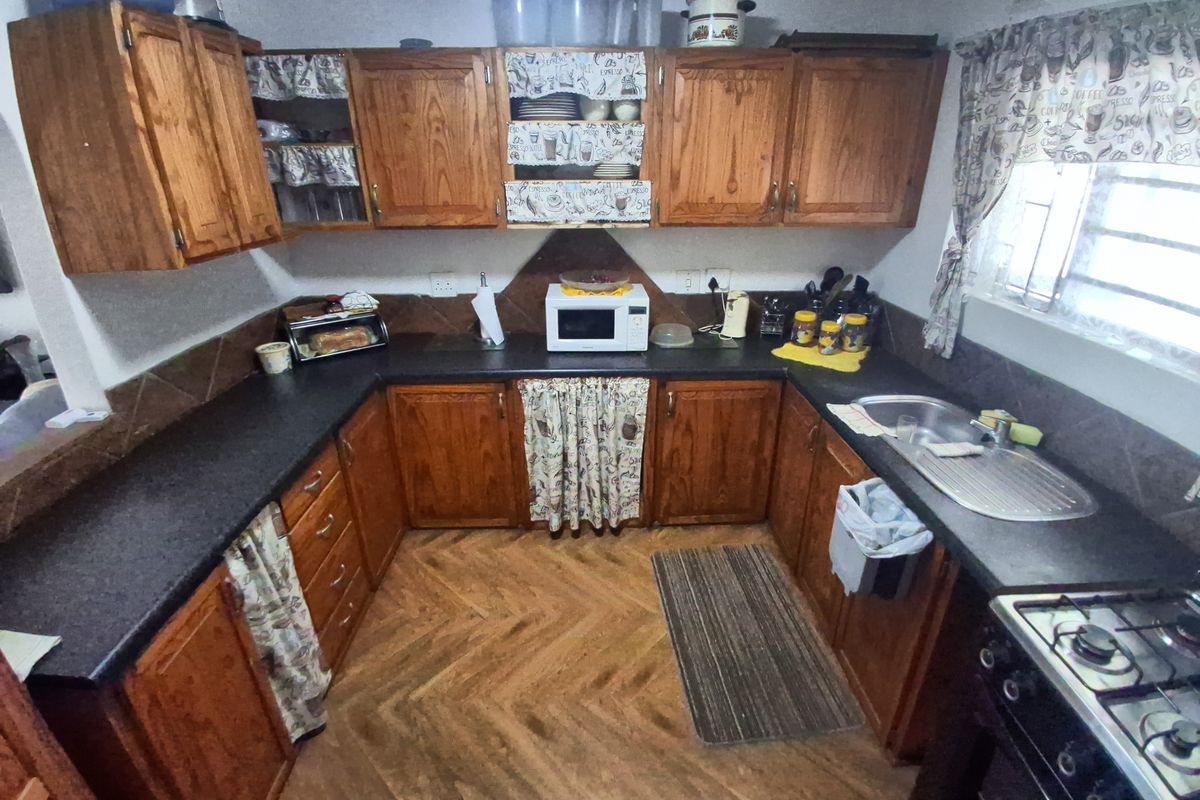 A functional U-shaped kitchen featuring traditional timber cabinetry, dark laminate countertops, a stainless steel sink, and a gas stove.