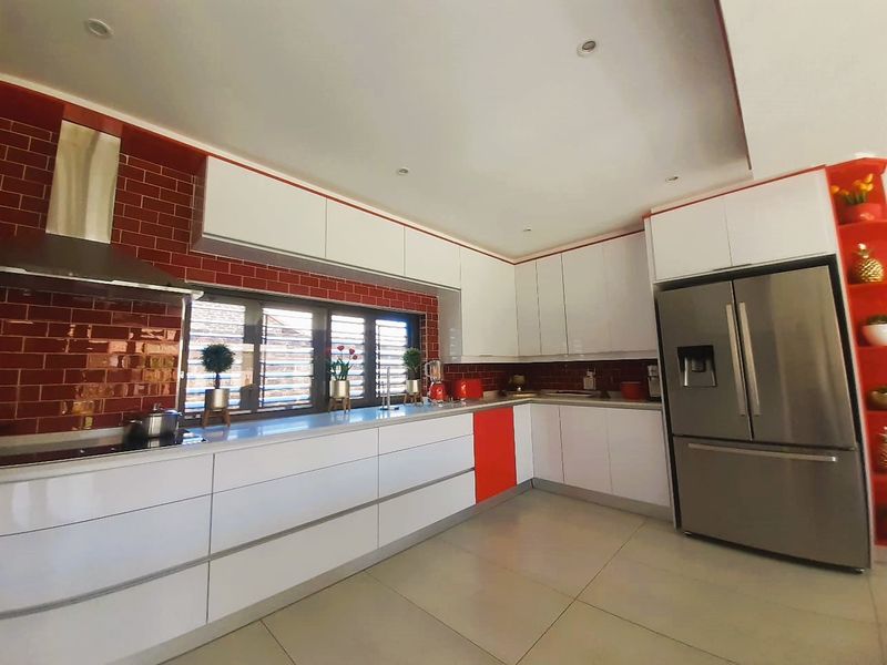 Modern kitchen featuring white cabinetry, red tiled splashback, stone countertops, and stainless steel extractor fan with integrated lighting.