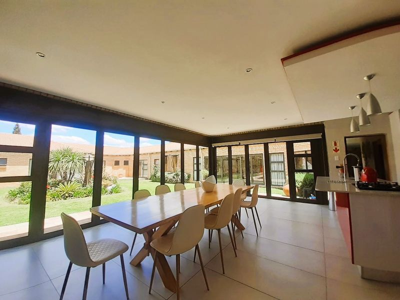 Spacious open-plan dining and kitchen area featuring large format floor tiles, recessed lighting, and extensive glass sliding doors providing seamless access to the garden.