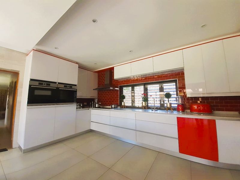 Modern kitchen featuring white and red cabinetry, built-in double ovens, a tiled splashback, and stone countertops with recessed lighting.