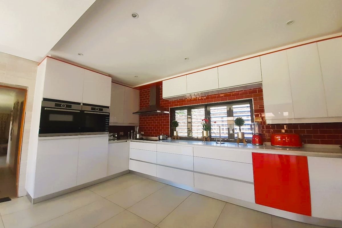 Modern kitchen featuring white and red cabinetry, built-in double ovens, a tiled splashback, and stone countertops with recessed lighting.