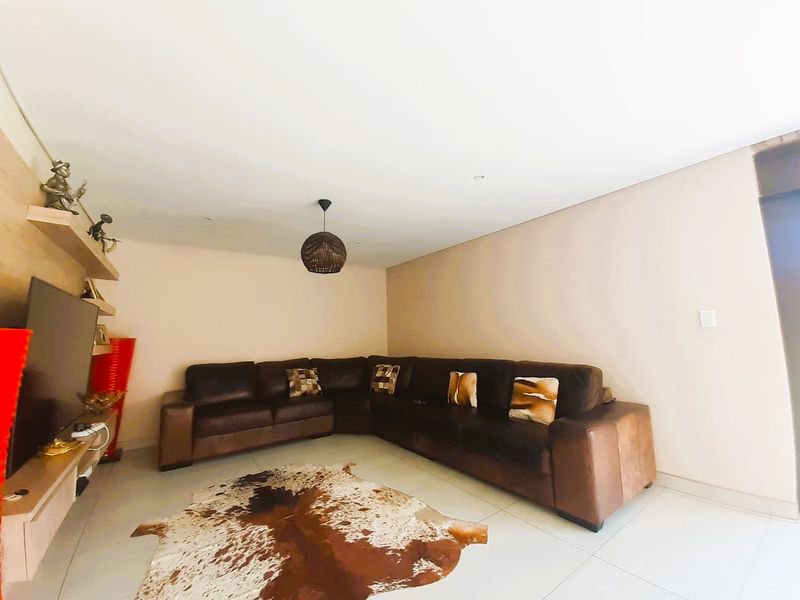 A well-maintained living room featuring neutral tiled flooring, recessed ceiling lighting, and a functional built-in shelving unit.