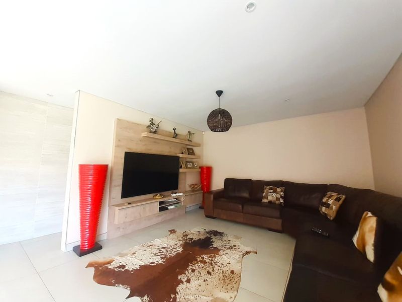 A comfortable living room featuring a modern built-in media unit, recessed ceiling lighting, and neutral tiled flooring.