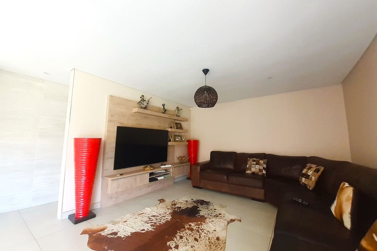 A comfortable living room featuring a modern built-in media unit, recessed ceiling lighting, and neutral tiled flooring.