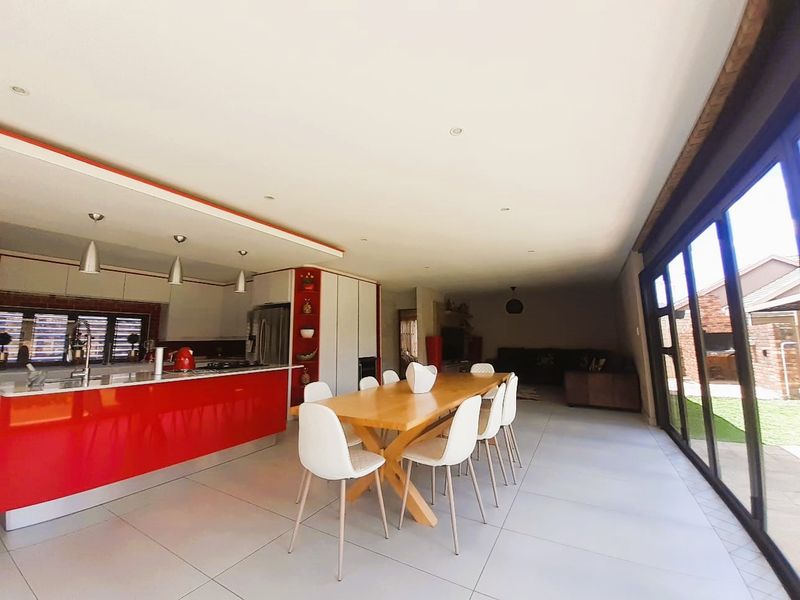 Spacious open-plan living and dining area featuring a modern kitchen with a red island, large format floor tiles, and expansive sliding doors to the garden.