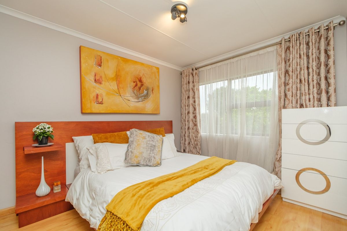 A well-maintained bedroom featuring a built-in wooden headboard, laminate flooring, and a large window allowing for natural light.