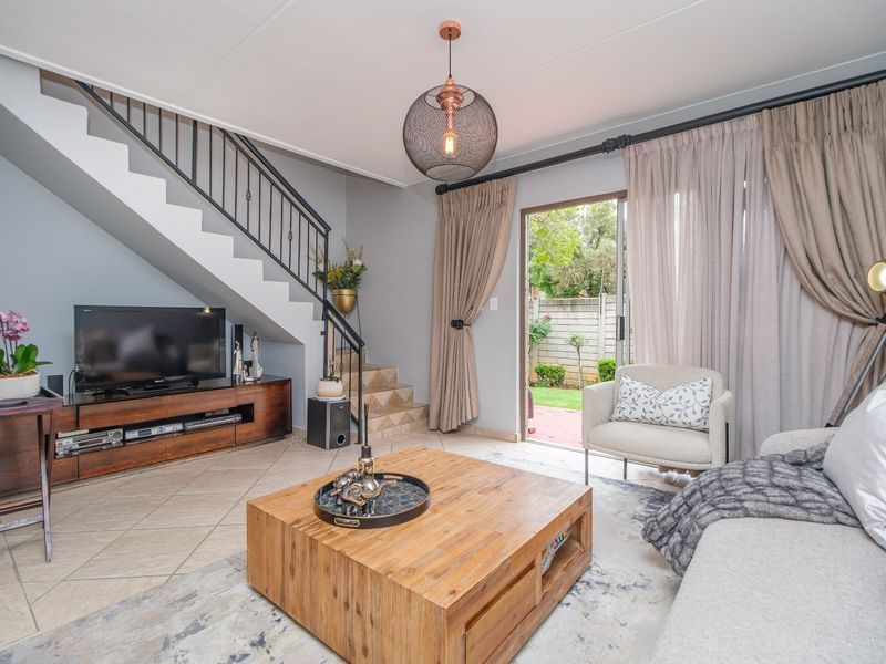 A well-maintained living room featuring a staircase with a wrought iron balustrade, tiled flooring, and a sliding glass door providing access to the garden.