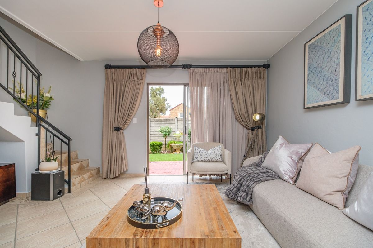 A well-maintained living room featuring tiled flooring, a staircase with a metal railing, and a sliding glass door providing access to the rear garden.