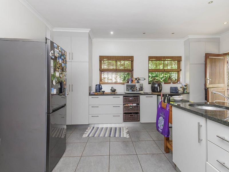 A functional kitchen featuring modern white cabinetry, granite countertops, tiled flooring, and direct access to the outdoor area through a timber door.
