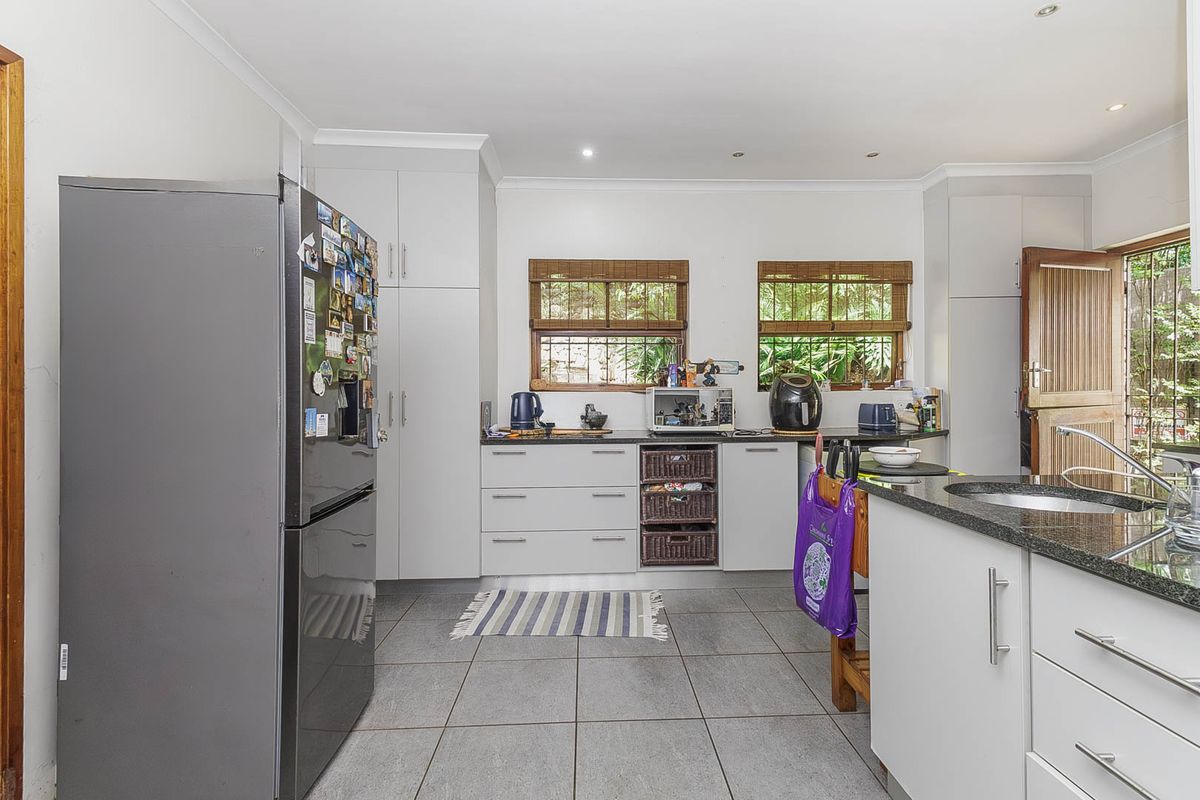 A functional kitchen featuring modern white cabinetry, granite countertops, tiled flooring, and direct access to the outdoor area through a timber door.