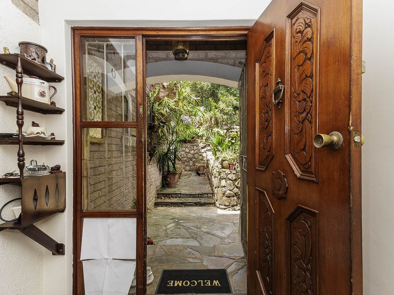 An inviting entryway featuring a detailed carved wooden door opening onto a stone-paved path leading to a lush, tiered garden area.