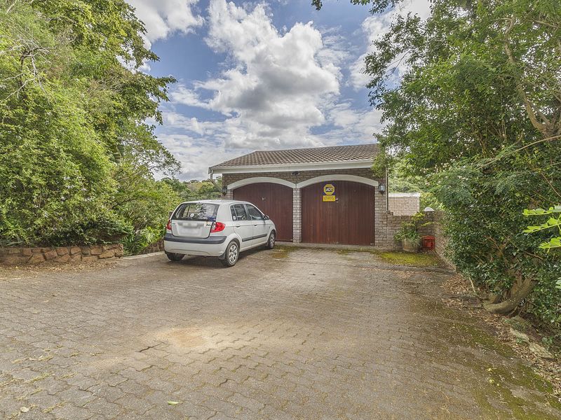 A detached double garage with wooden doors, featuring a paved driveway and surrounded by mature trees and landscaping.