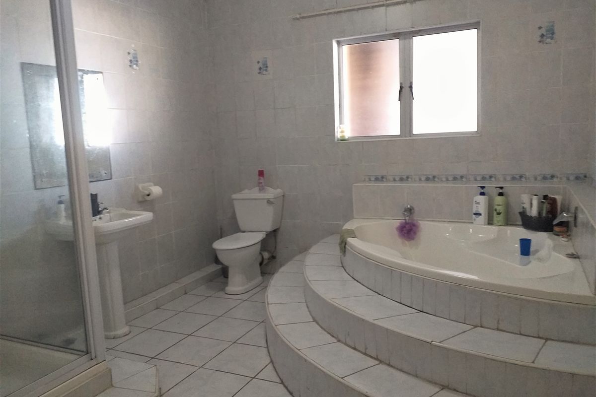 Spacious bathroom featuring a raised corner soaking tub, separate glass-enclosed shower, pedestal basin, and toilet with neutral wall and floor tiling.