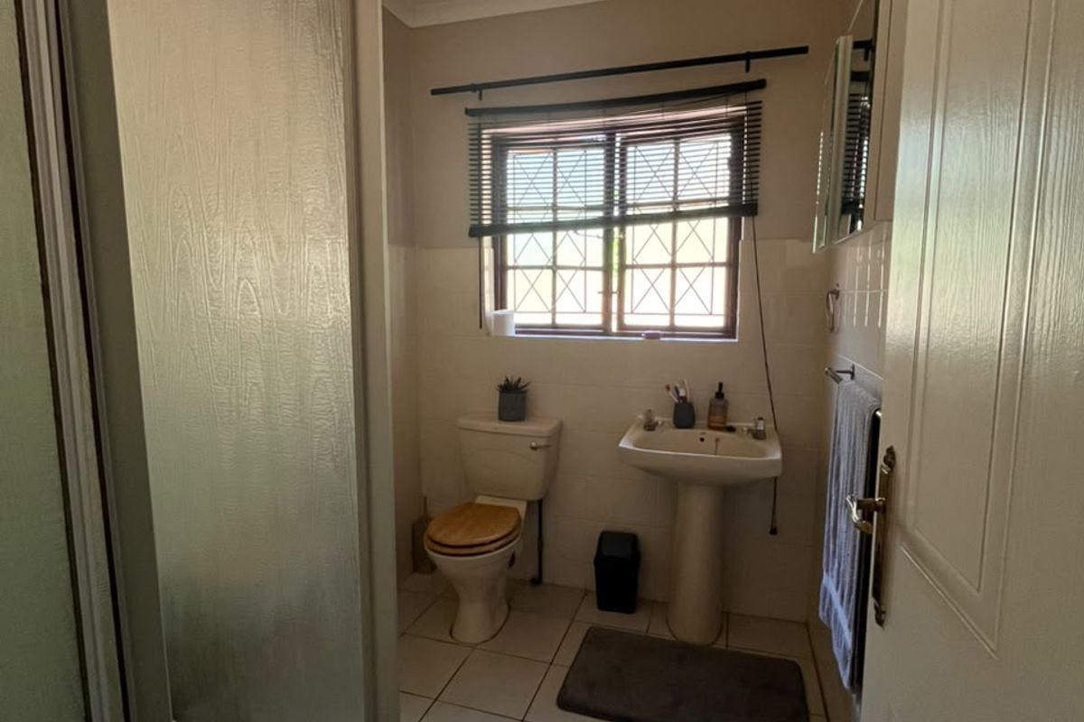 A functional bathroom featuring a pedestal basin, toilet, and a shower enclosure with tiled flooring and security bars on the window.
