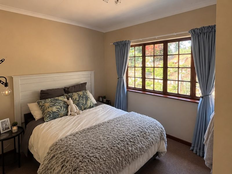A cozy bedroom featuring timber-framed windows with garden views and neutral wall tones, providing a comfortable and well-maintained living space.