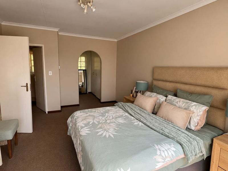 A well-maintained bedroom featuring neutral wall tones, carpeted flooring, a decorative archway leading to an adjacent space, and classic cove cornicing.
