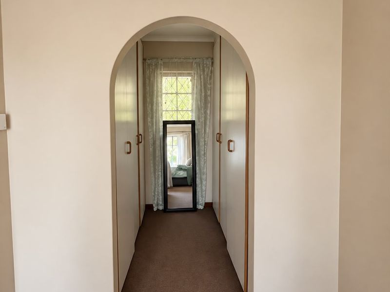 A hallway featuring an arched entryway leading to a corridor with built-in cupboards and a window at the end.