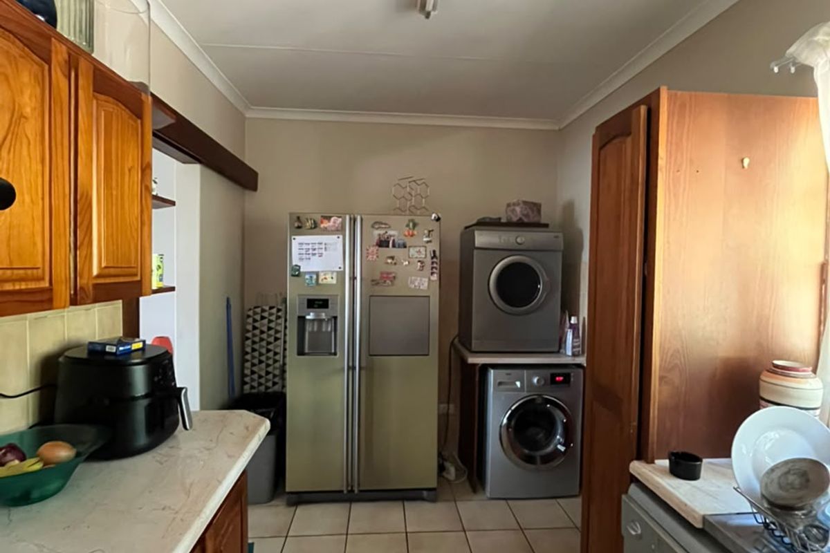 A functional kitchen featuring wooden cabinetry, tiled flooring, and integrated appliance space, offering a practical layout with potential for modern updates.