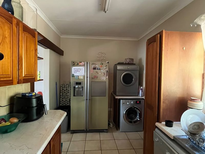 A functional kitchen featuring wooden cabinetry, tiled flooring, and integrated appliance space, offering a practical layout with potential for modern updates.