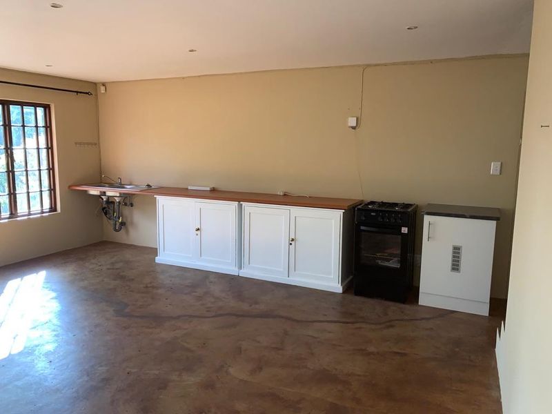 A functional kitchen area featuring built-in cabinetry, a gas stove, and a stainless steel sink, set against a neutral backdrop with concrete flooring.