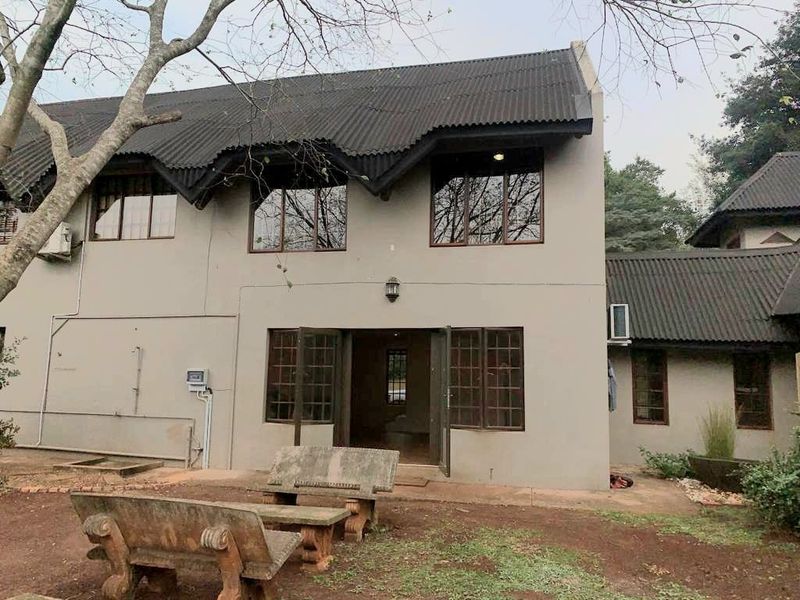 Rear view of a two-story cottage featuring a corrugated metal roof, timber-framed windows, and double door access to the garden area.