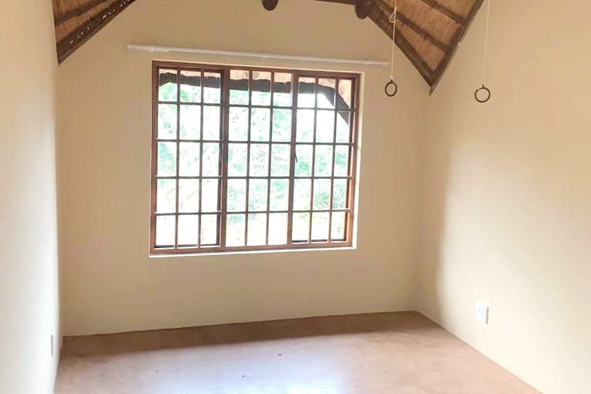 A vacant bedroom featuring a high vaulted thatched ceiling with exposed timber rafters, timber-framed windows, and a concrete floor.