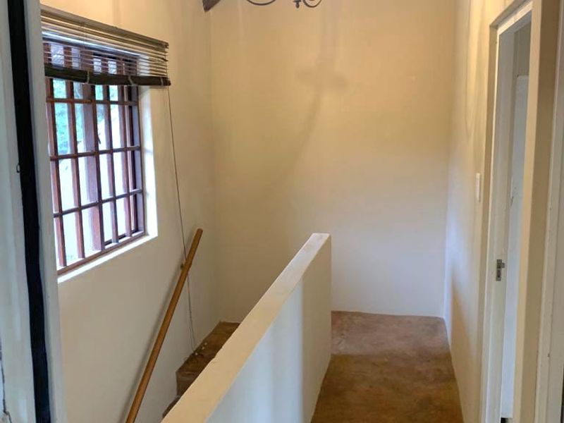 A bright hallway featuring exposed timber rafters, a thatched ceiling, and a solid wall balustrade overlooking the staircase area.