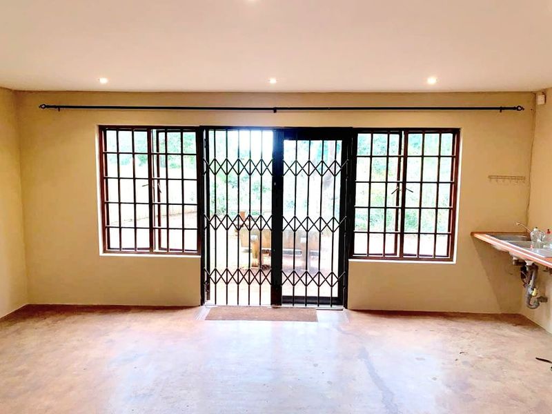 An open-plan living area featuring concrete flooring, recessed lighting, and a basic kitchen sink area with security bars on the windows and door.