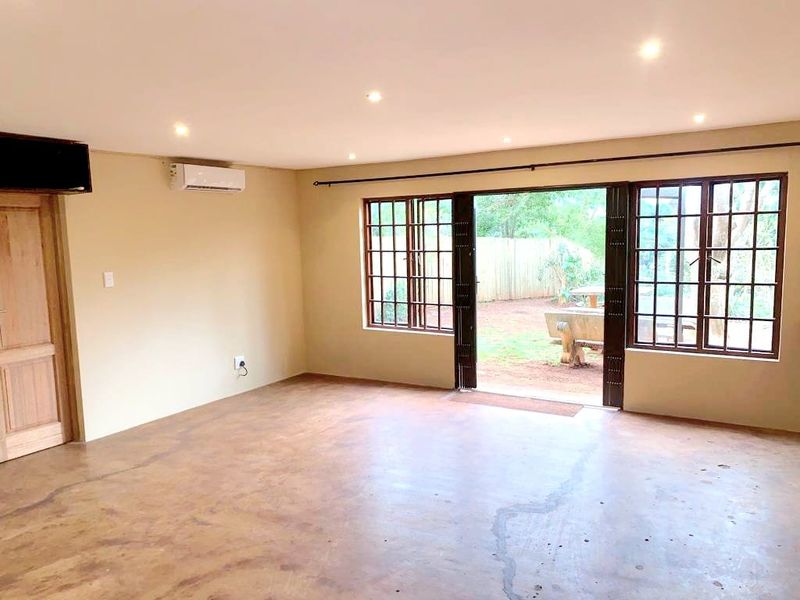 Spacious living area featuring concrete flooring, recessed lighting, and a split-system air conditioner, with direct access to the rear garden through large grid-pattern windows.