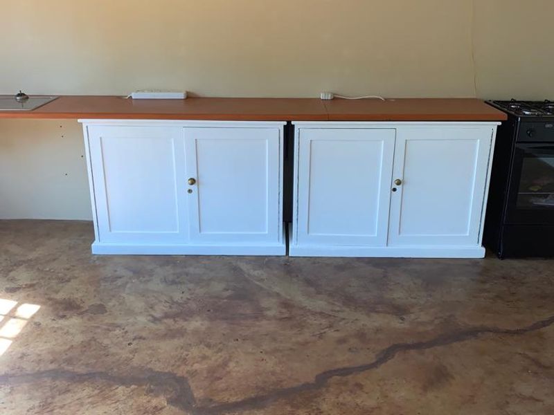 A functional kitchen area featuring white built-in cabinetry, a laminate countertop, a freestanding oven, and a polished concrete floor.