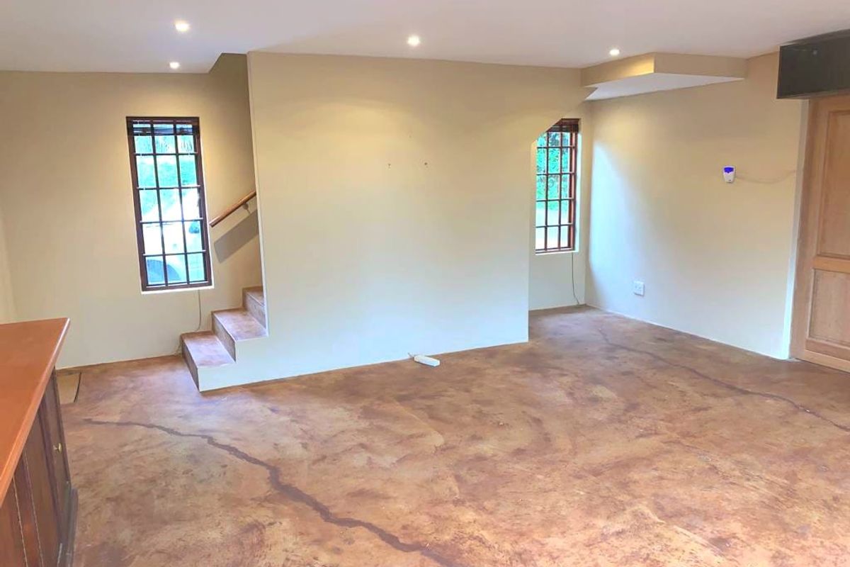 An open-plan living area featuring concrete flooring, recessed lighting, and a staircase, offering a blank canvas for interior design.