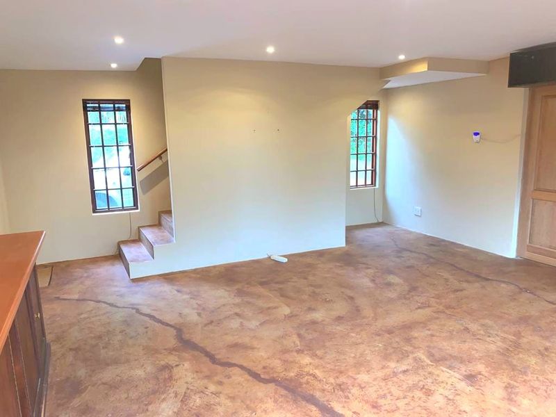 An open-plan living area featuring concrete flooring, recessed lighting, and a staircase, offering a blank canvas for interior design.