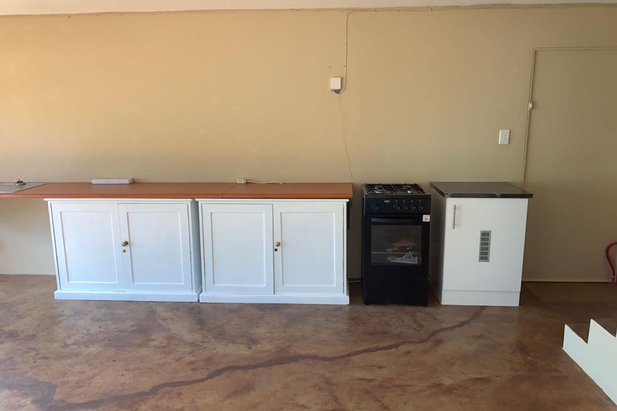 A basic kitchen area featuring white cabinetry, a freestanding stove, and concrete flooring, offering a functional space ready for modernization and aesthetic updates.
