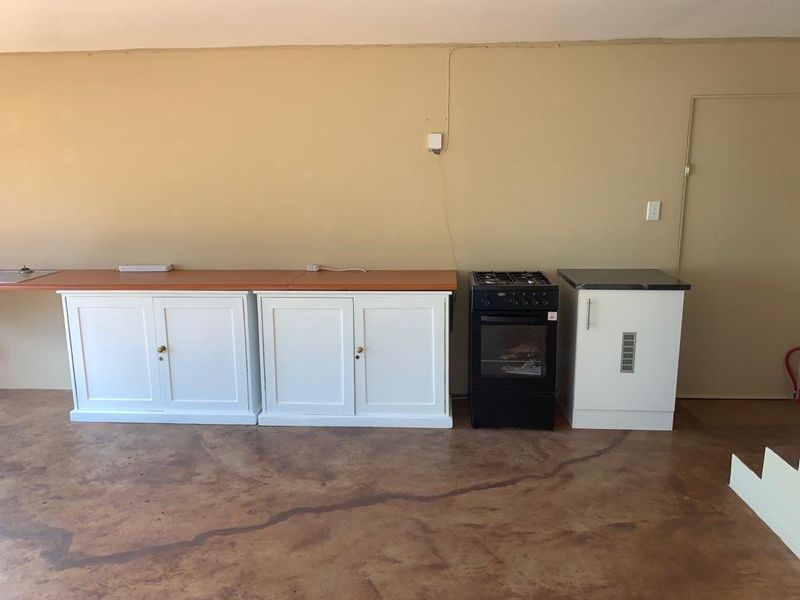 A basic kitchen area featuring white cabinetry, a freestanding stove, and concrete flooring, offering a functional space ready for modernization and aesthetic updates.